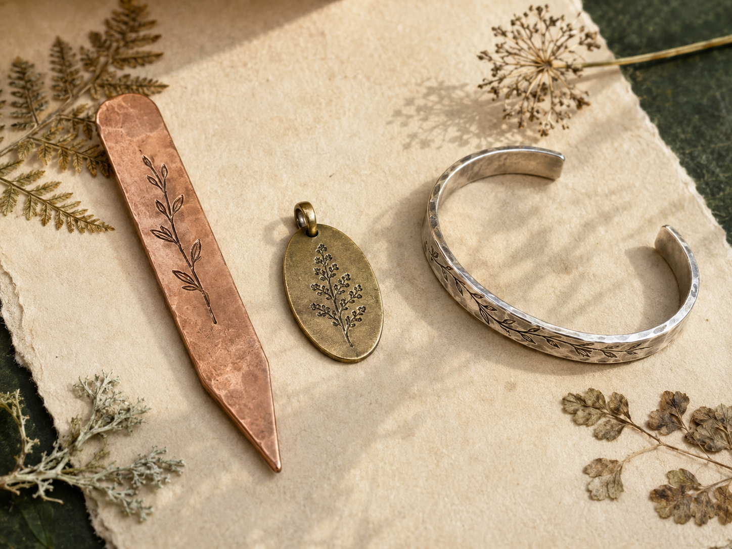 Copper garden marker, brass pendant, and silver botanical cuff with pressed herbs