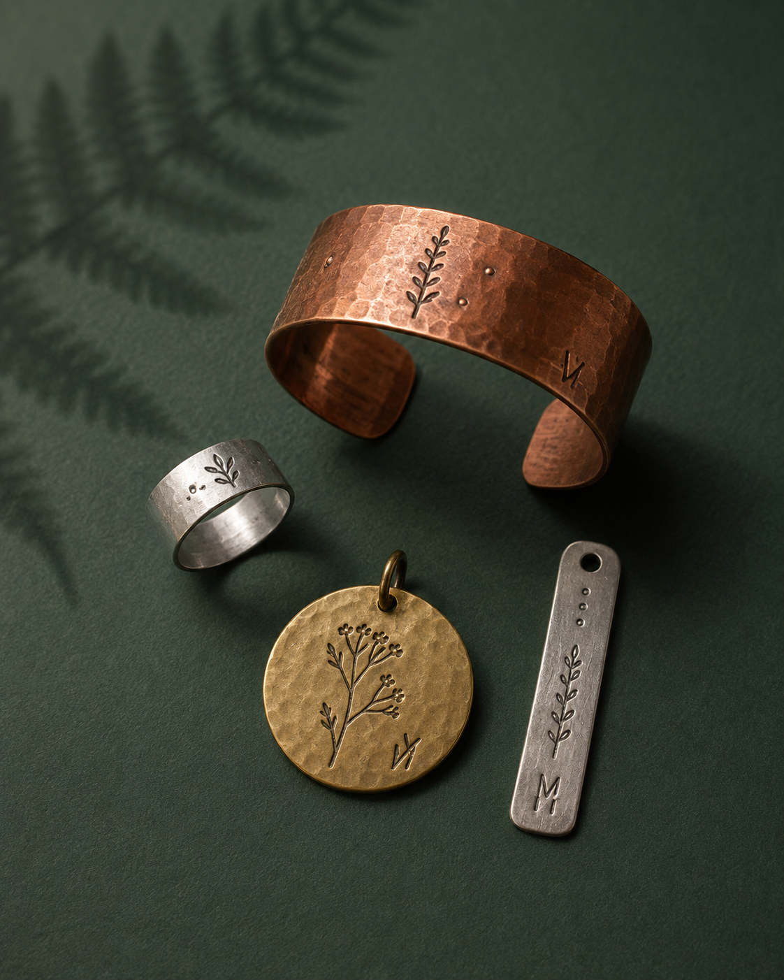 Hand-stamped copper, silver, and brass jewelry on deep forest green paper